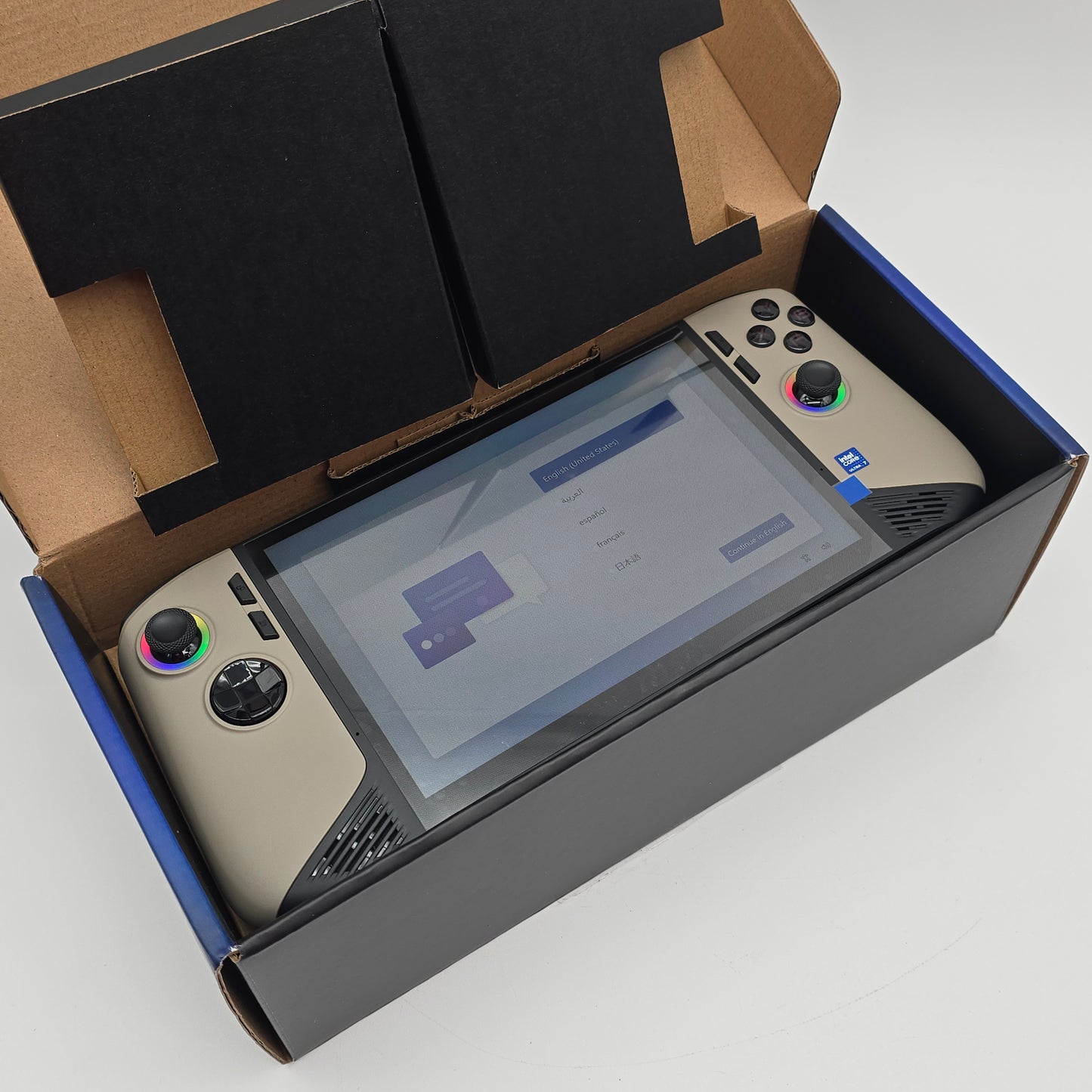 Gaming console with screen and controller in an open cardboard box on a light gray background