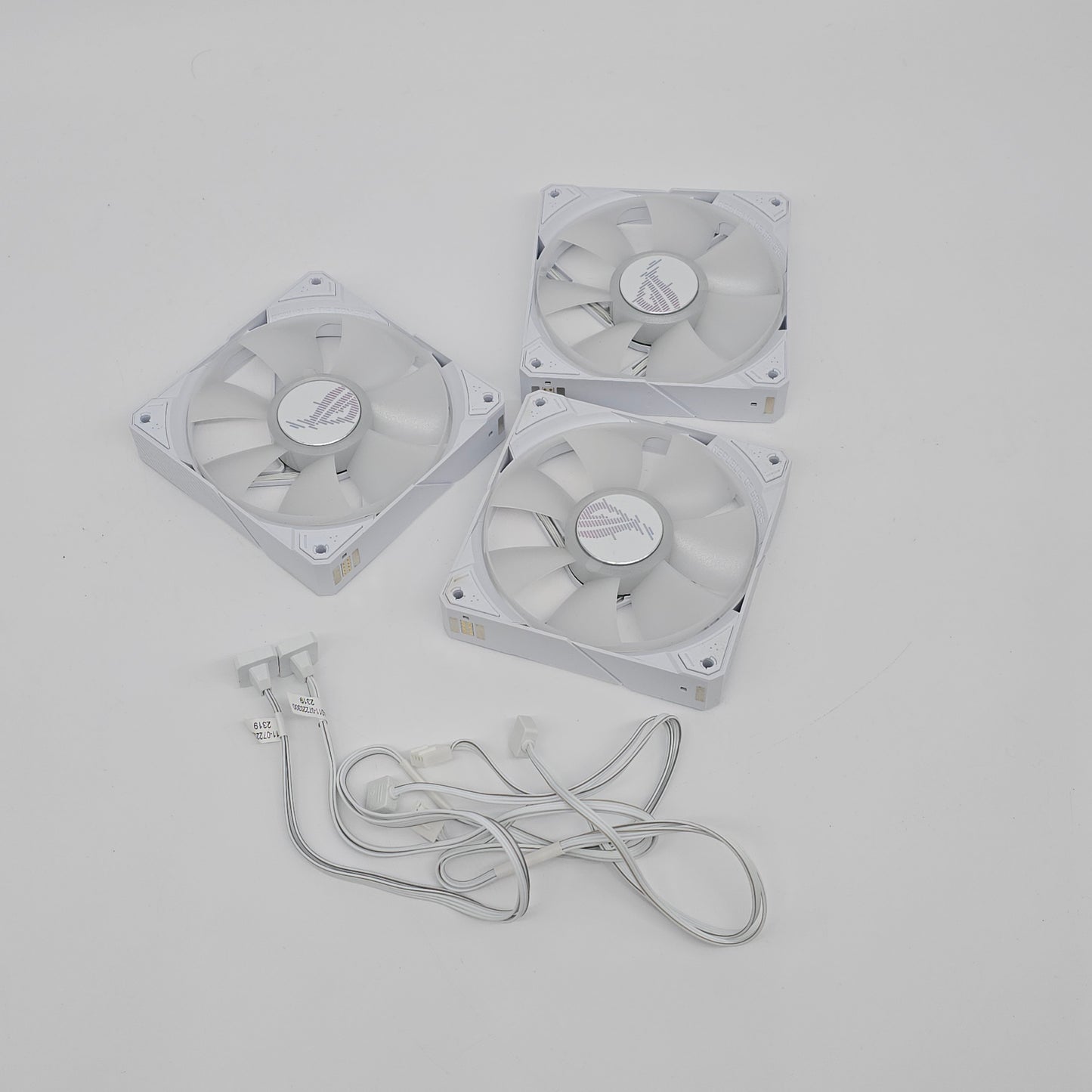 Three white computer fans with a power cable on a light gray background asus rog strix